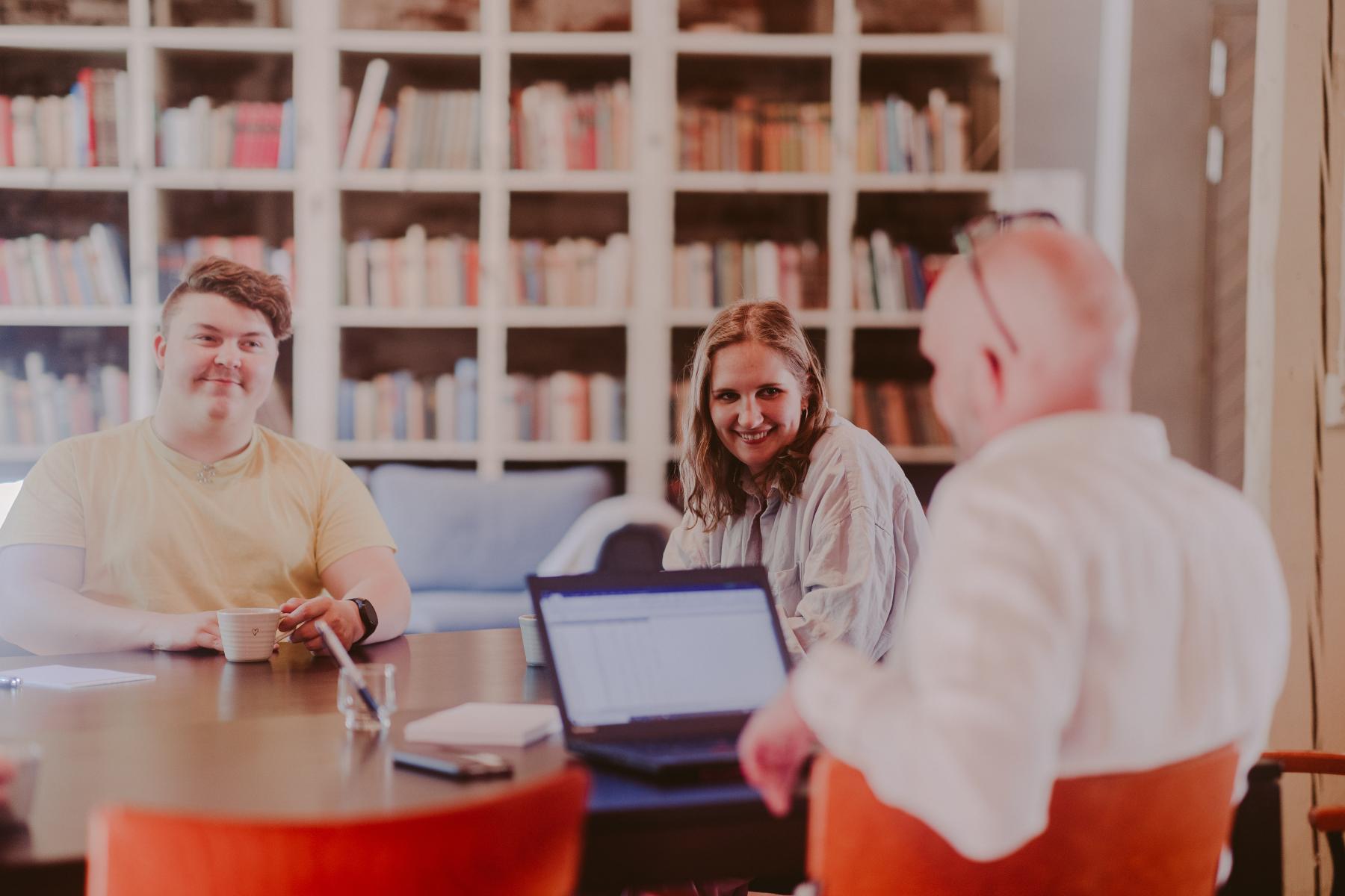 Kolme iloista henkilöä pitämässä kokousta vanhan ruukkirakennuksen kokoustilassa.