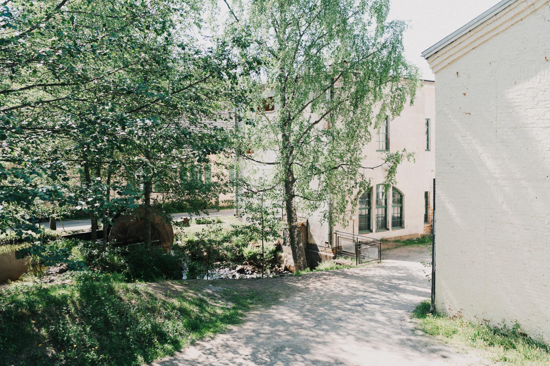 Mathildedalin kylänäkymä, joka esittää joen yllä olevaa lehvästöä ja myllyn pyörää.