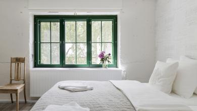 Hotel Mathildedalin hotellihuone, jossa pedatut sängyt, vihreäkarminen ikkunan ja kukkia ikkunalaudalla.